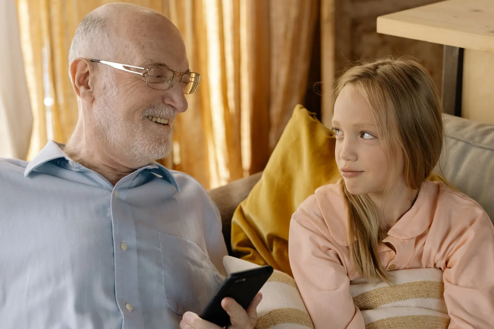 A grandfather and his granddaughter talking on the sofa at home