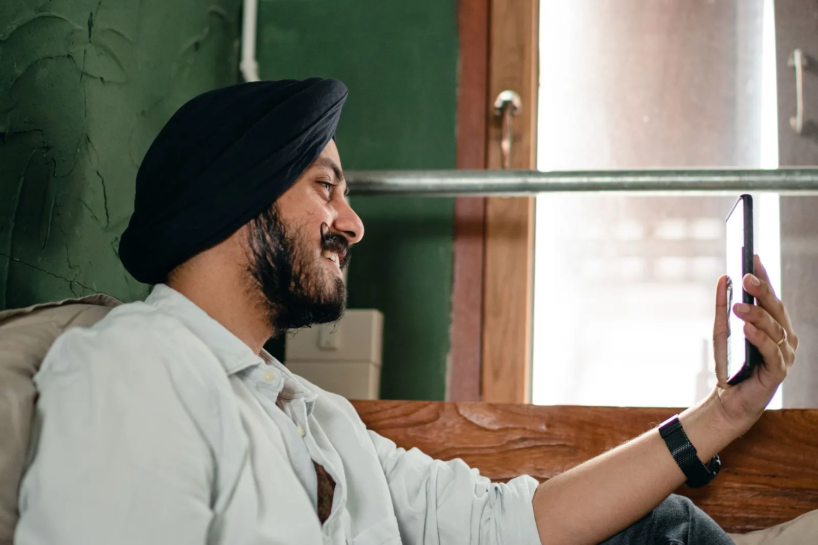 A smiling man in a turban on a video call on his phone at home