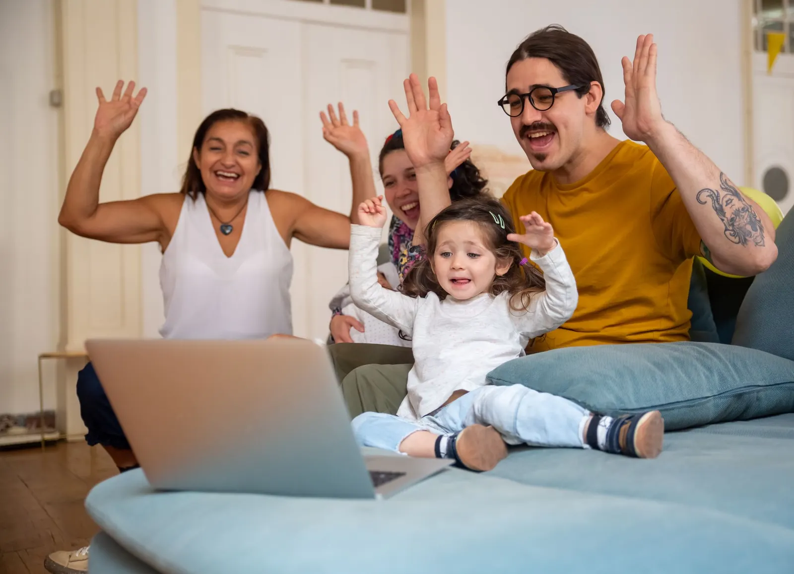 A grandmother, parents and a toddler waving at a laptop call with family far away
