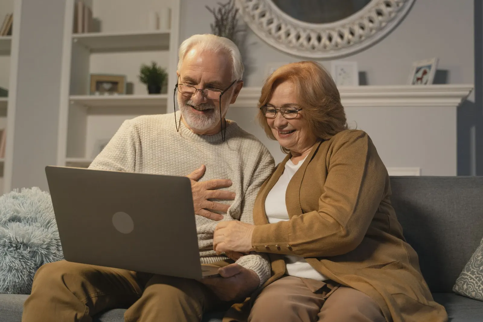 An older couple on a sofa, laughing as they talk to family on a video call